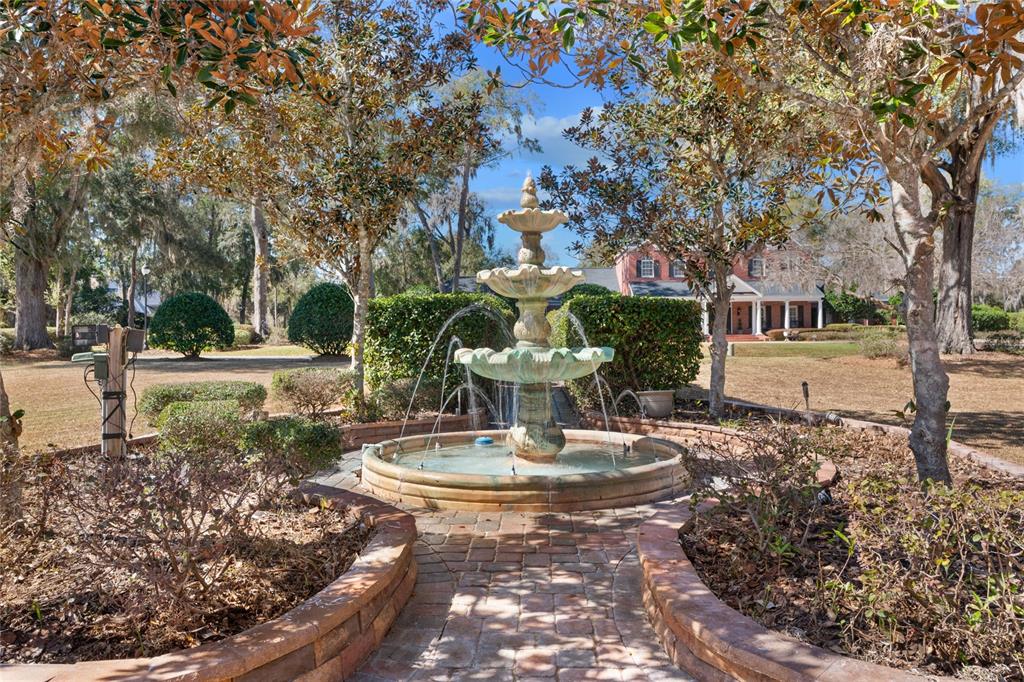 A three-tiered stone fountain sits in a brick-paved garden area in front of a house — 3409 SE 17TH COURT, OCALA, FL