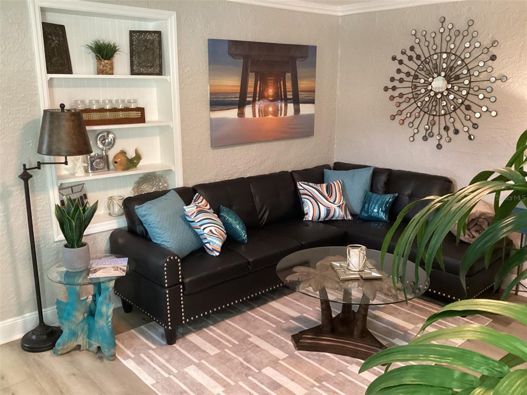 A living room features a black sectional sofa, a glass coffee table, and built-in shelving — 13121 4TH STREET E UNIT 2, MADEIRA BEACH, FL