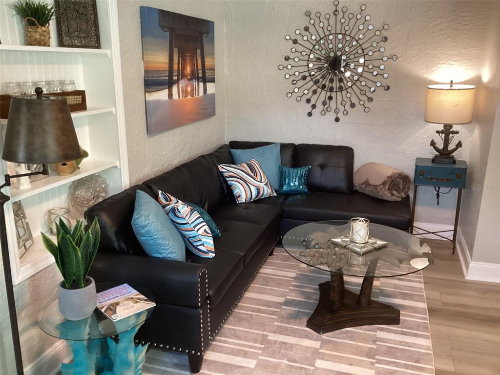 A living room features a black sectional sofa, a glass coffee table, and coastal decor — 13121 4TH STREET E UNIT 2, MADEIRA BEACH, FL