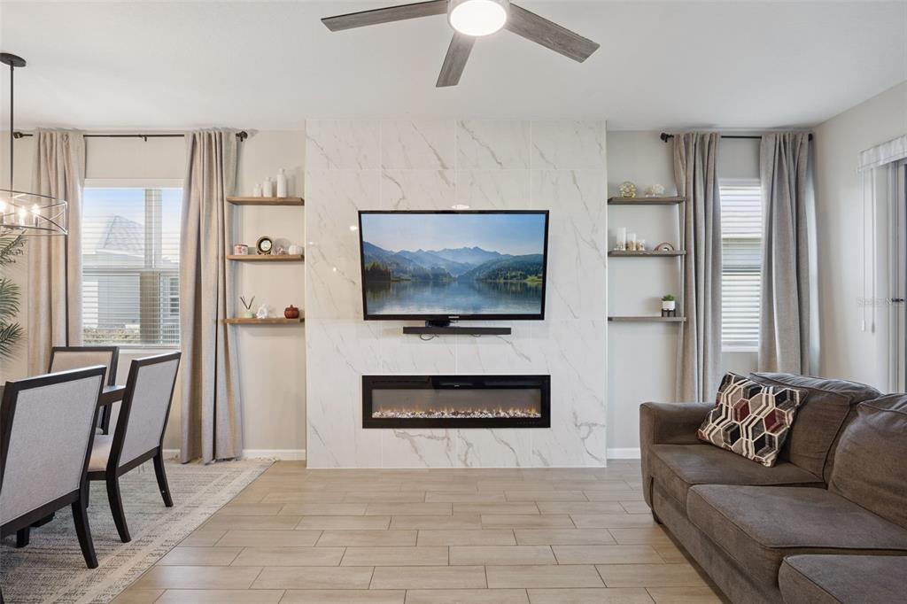 A living room features a marble-tiled fireplace wall with a mounted television and floating shelves — 10053 SPRING LAKE DRIVE, CLERMONT, FL