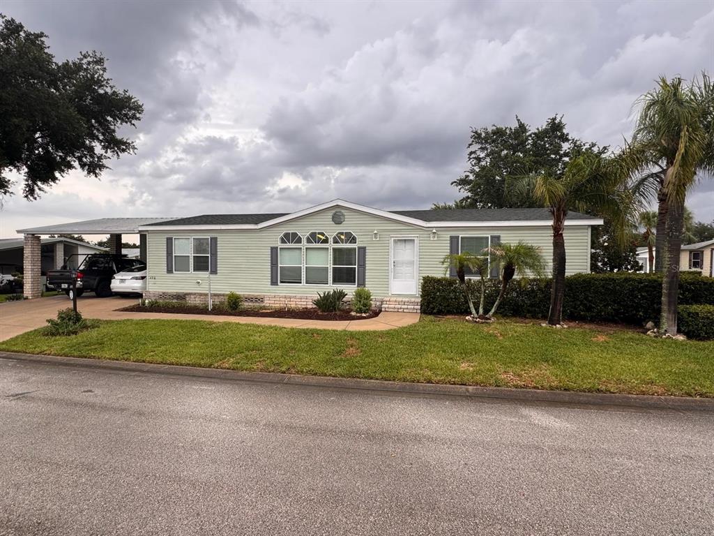 A light green manufactured home features a covered carport, a front lawn, and palm trees — 406 WINDMILL BLVD, DAVENPORT, FL