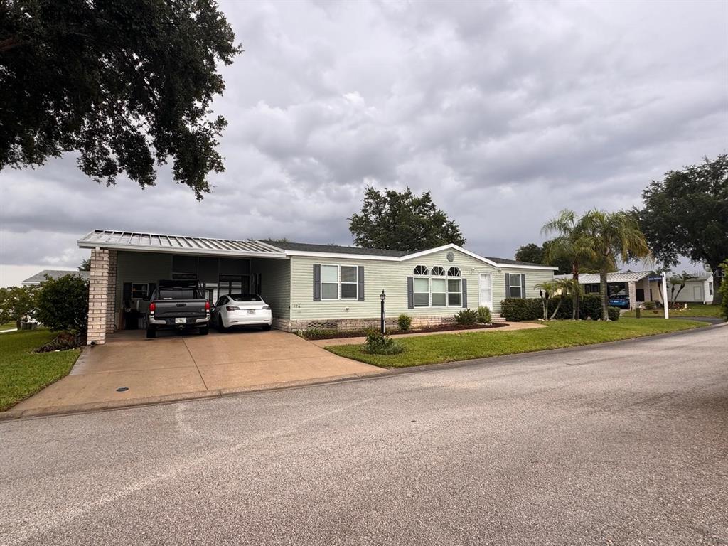 A light green manufactured home features a carport, a concrete driveway, and a front lawn — 406 WINDMILL BLVD, DAVENPORT, FL