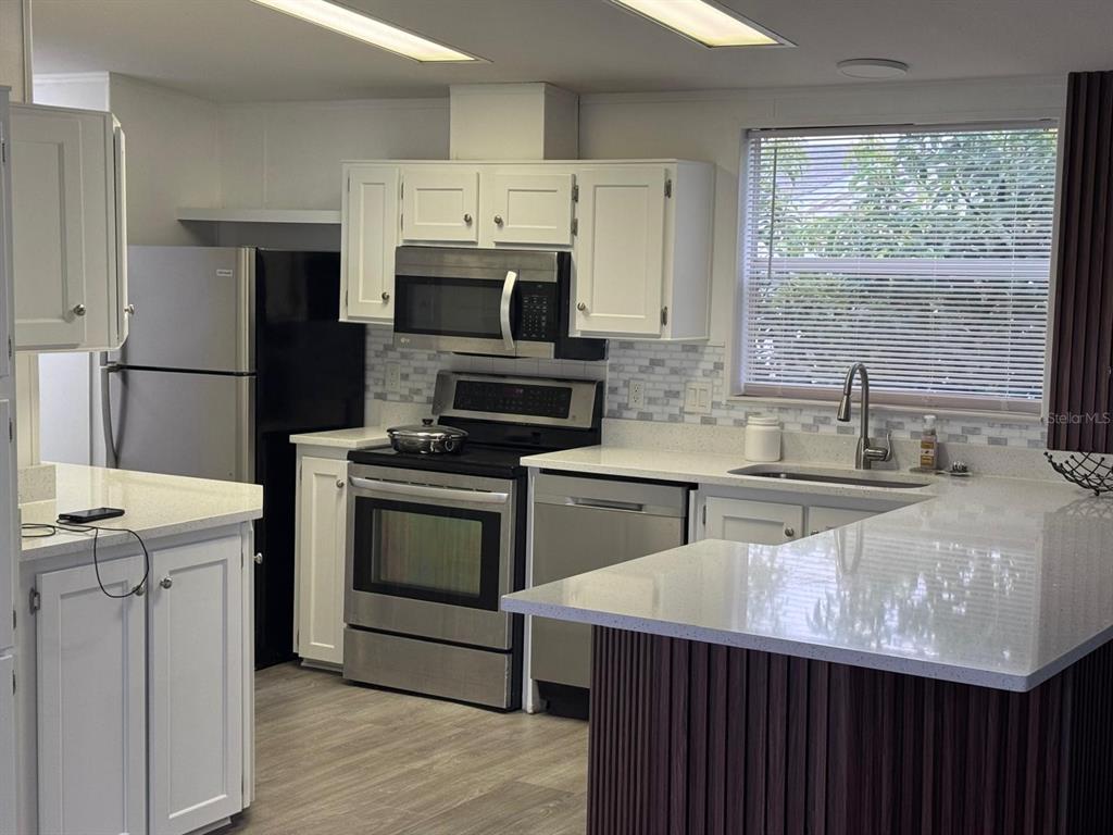 A kitchen features white cabinets, stainless steel appliances, quartz countertops, and a dark wood island — 406 WINDMILL BLVD, DAVENPORT, FL
