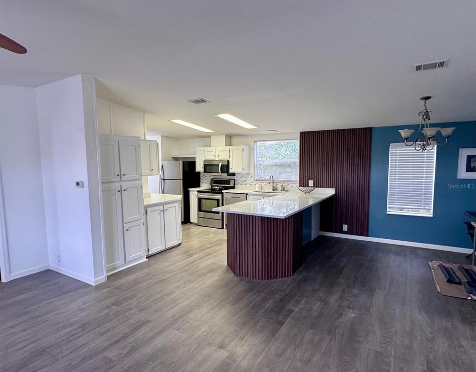 A kitchen with white cabinets, stainless steel appliances, and a dark wood-paneled island — 406 WINDMILL BLVD, DAVENPORT, FL