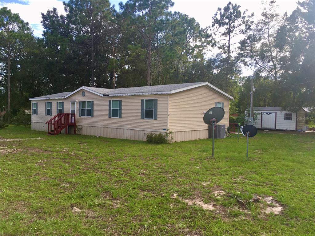 A tan manufactured home with a red wooden staircase sits on a grassy lot — 5990 NE 101ST AVE, BRONSON, FL