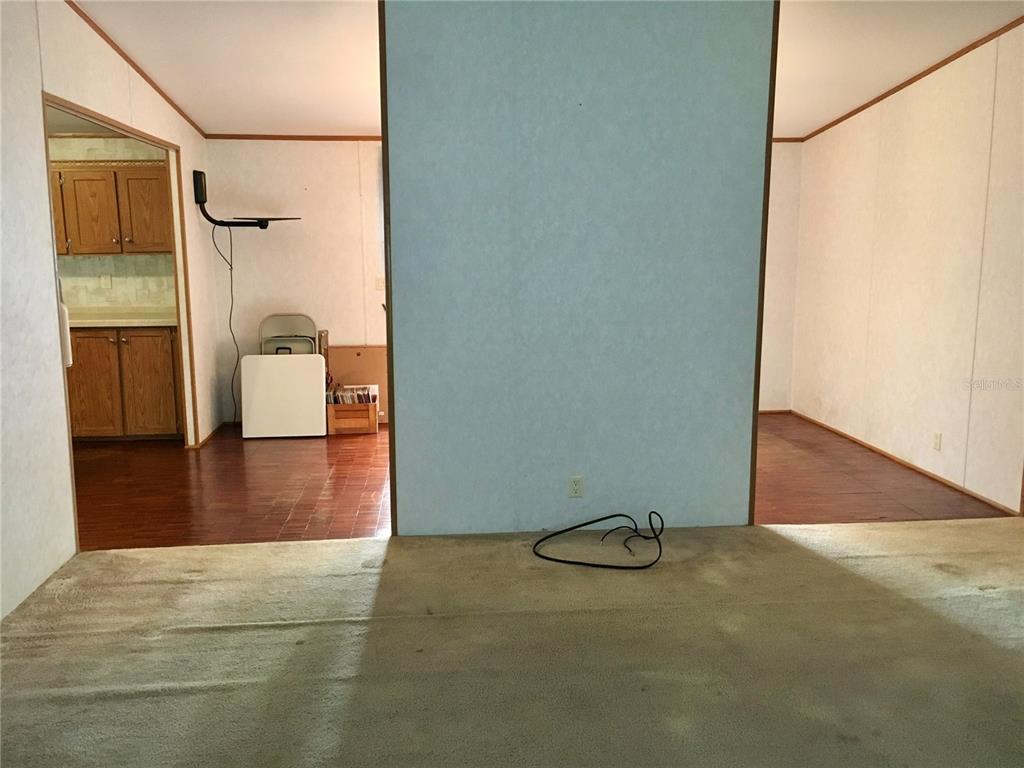 A carpeted living area opens to a kitchen and another room with wood-look flooring — 5990 NE 101ST AVE, BRONSON, FL