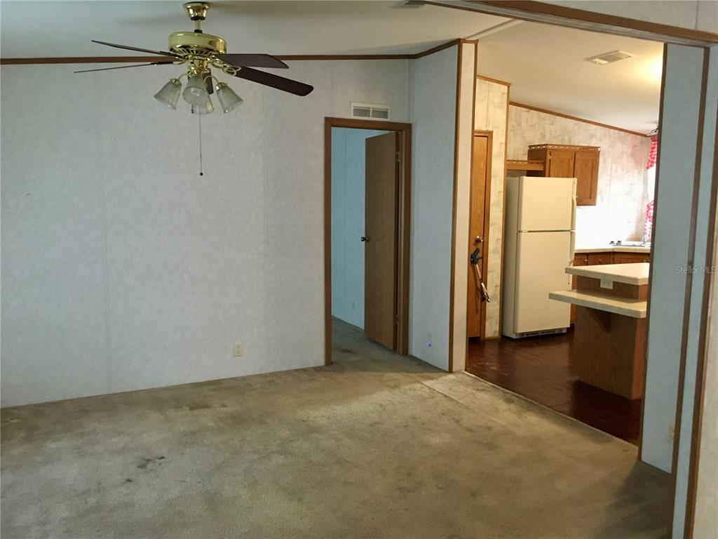 A carpeted living room leads into a kitchen with a white refrigerator and wood cabinets — 5990 NE 101ST AVE, BRONSON, FL
