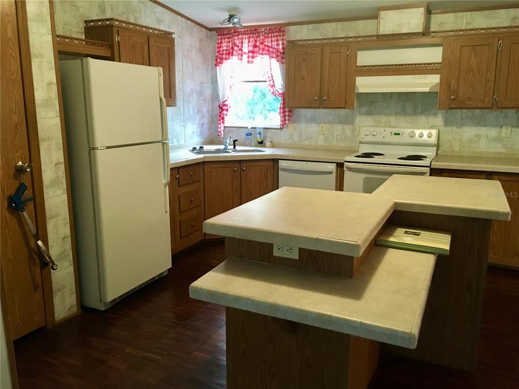 A kitchen features wood cabinets, a white refrigerator, a tiled island, and a corner sink — 5990 NE 101ST AVE, BRONSON, FL