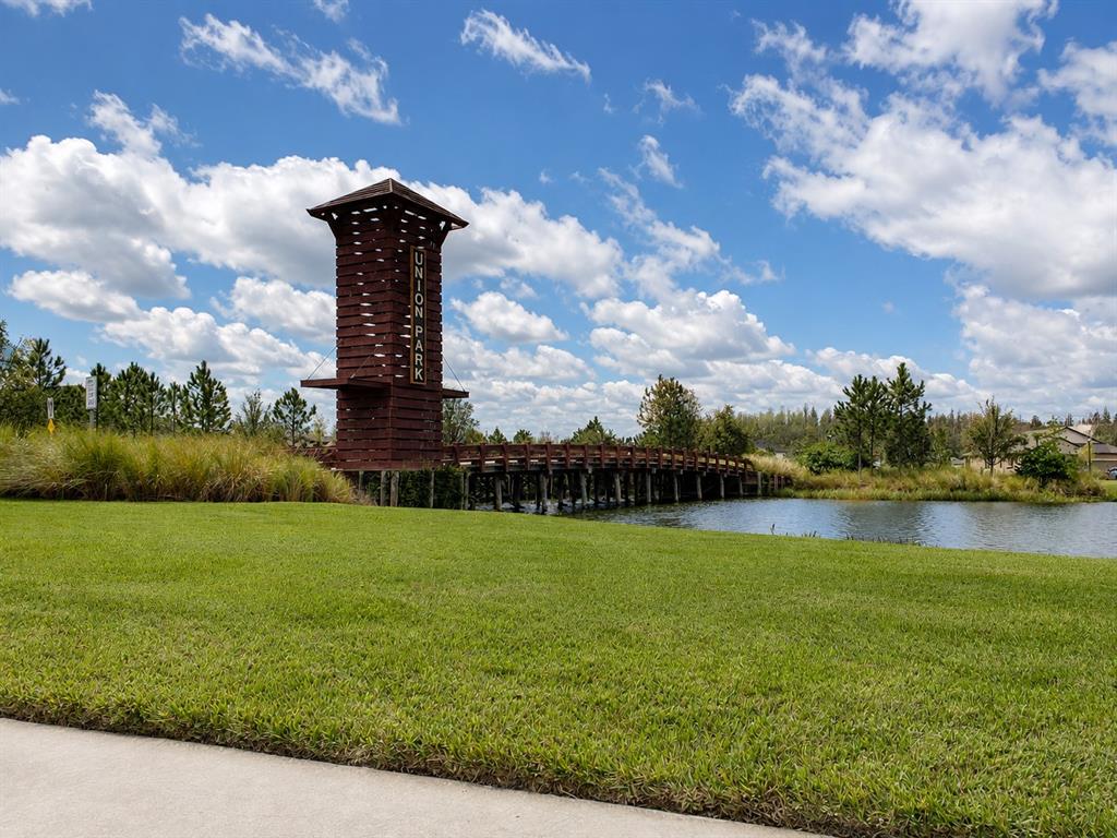 A wooden tower and footbridge stand beside a pond in a grassy park area — 1652 HUBBELL ROAD, WESLEY CHAPEL, FL