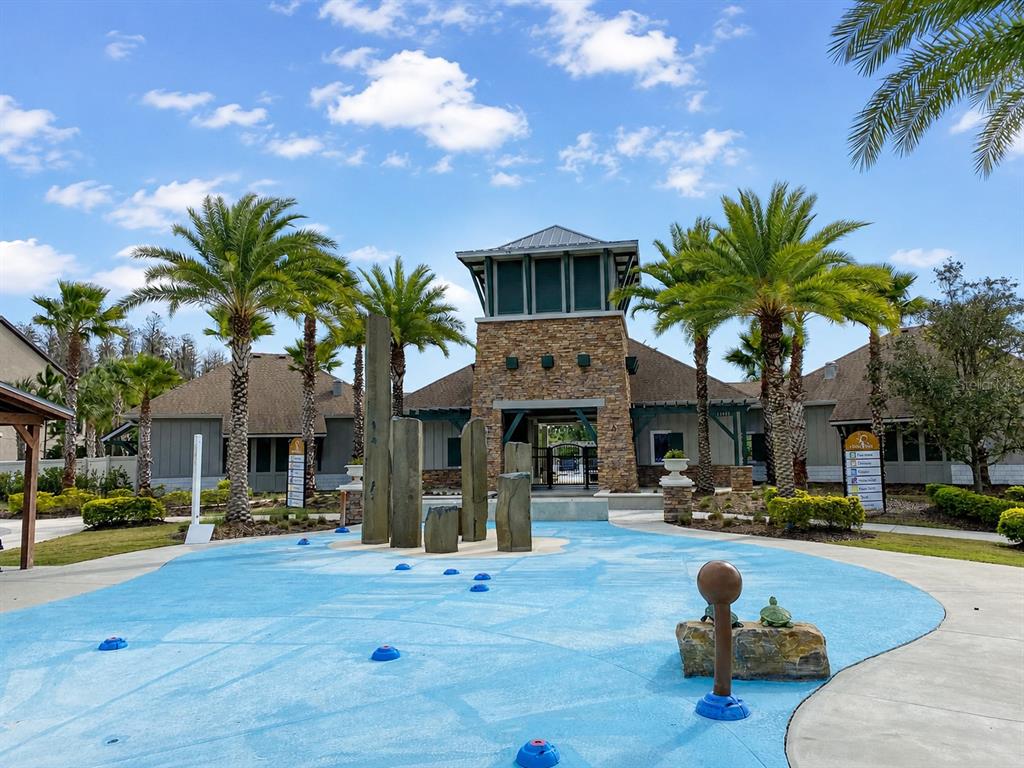 A blue splash pad with stone pillars sits in front of a community clubhouse building — 1652 HUBBELL ROAD, WESLEY CHAPEL, FL