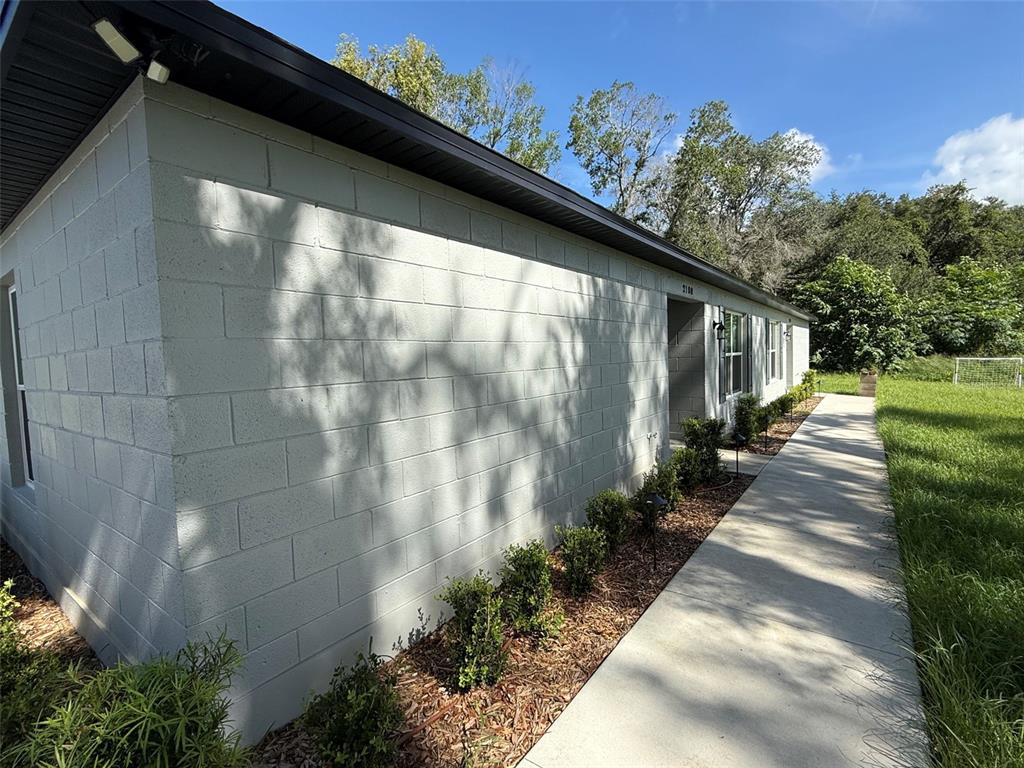 A light-colored concrete block house exterior features a long sidewalk and small landscaping shrubs — 2108 SOUTH STREET, LEESBURG, FL