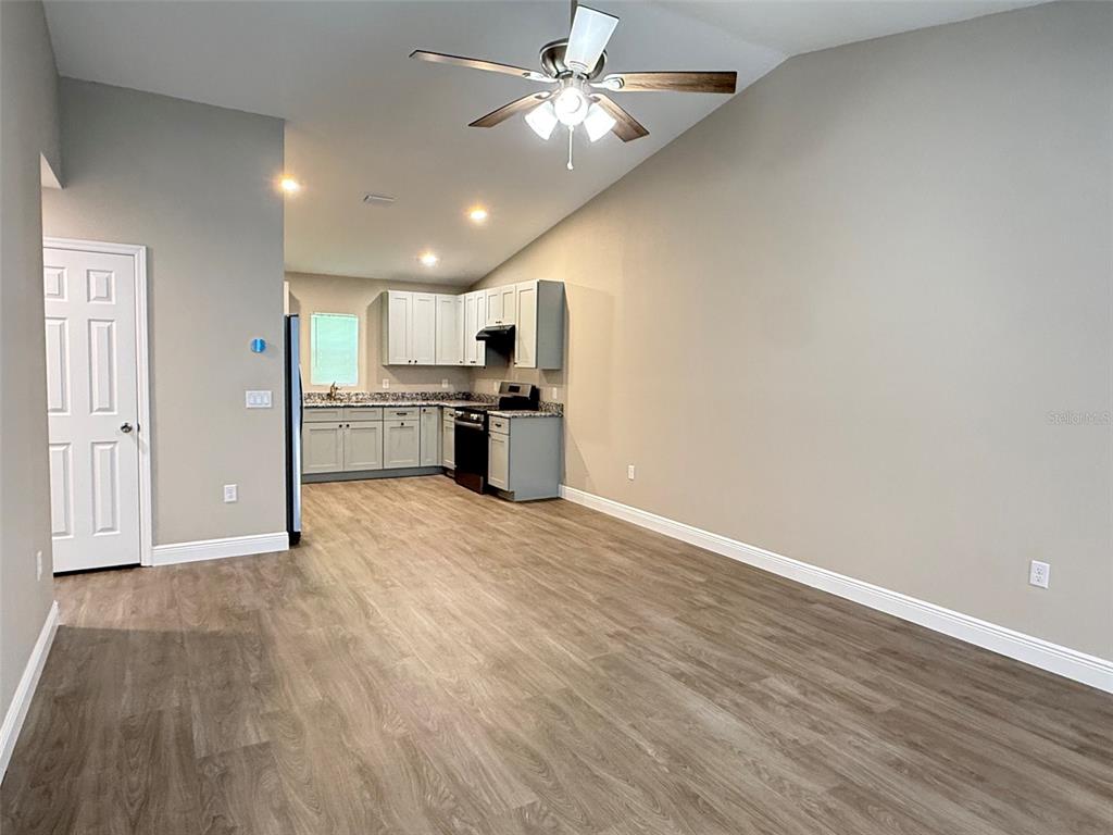An open-concept kitchen features light gray cabinets, granite countertops, and wood-look flooring — 2108 SOUTH STREET, LEESBURG, FL