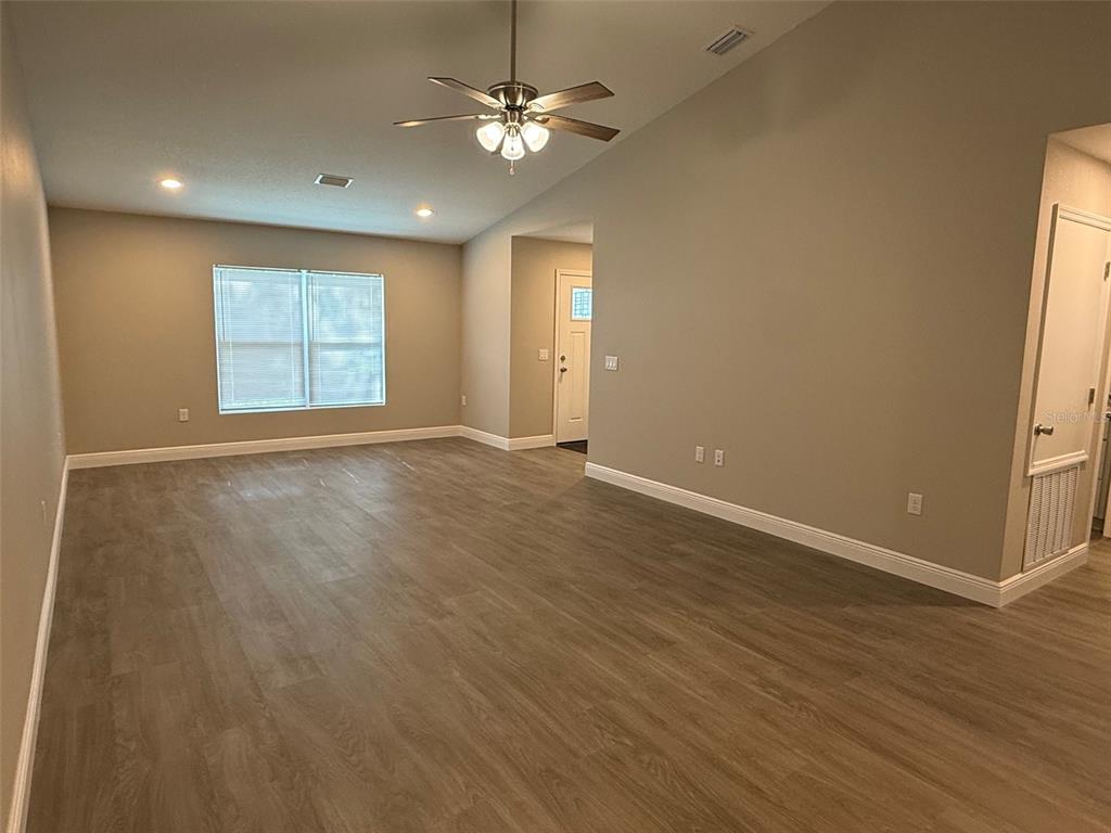 An empty living room with light-colored walls, wood-look flooring, a ceiling fan, and a window — 2108 SOUTH STREET, LEESBURG, FL