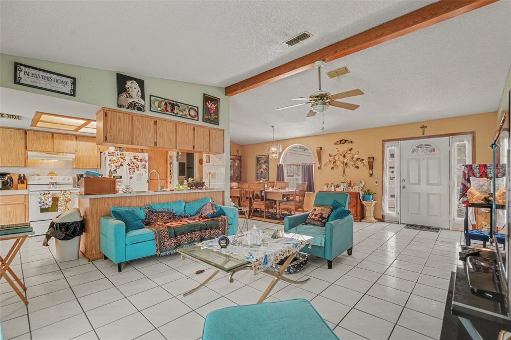An open-concept living room and kitchen feature white tile floors, teal furniture, and wood cabinets — 4589 MARINER BLVD, SPRING HILL, FL