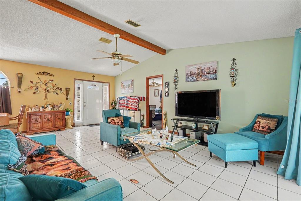 A living room features light tile floors, a vaulted ceiling with wood beams, and teal furniture — 4589 MARINER BLVD, SPRING HILL, FL