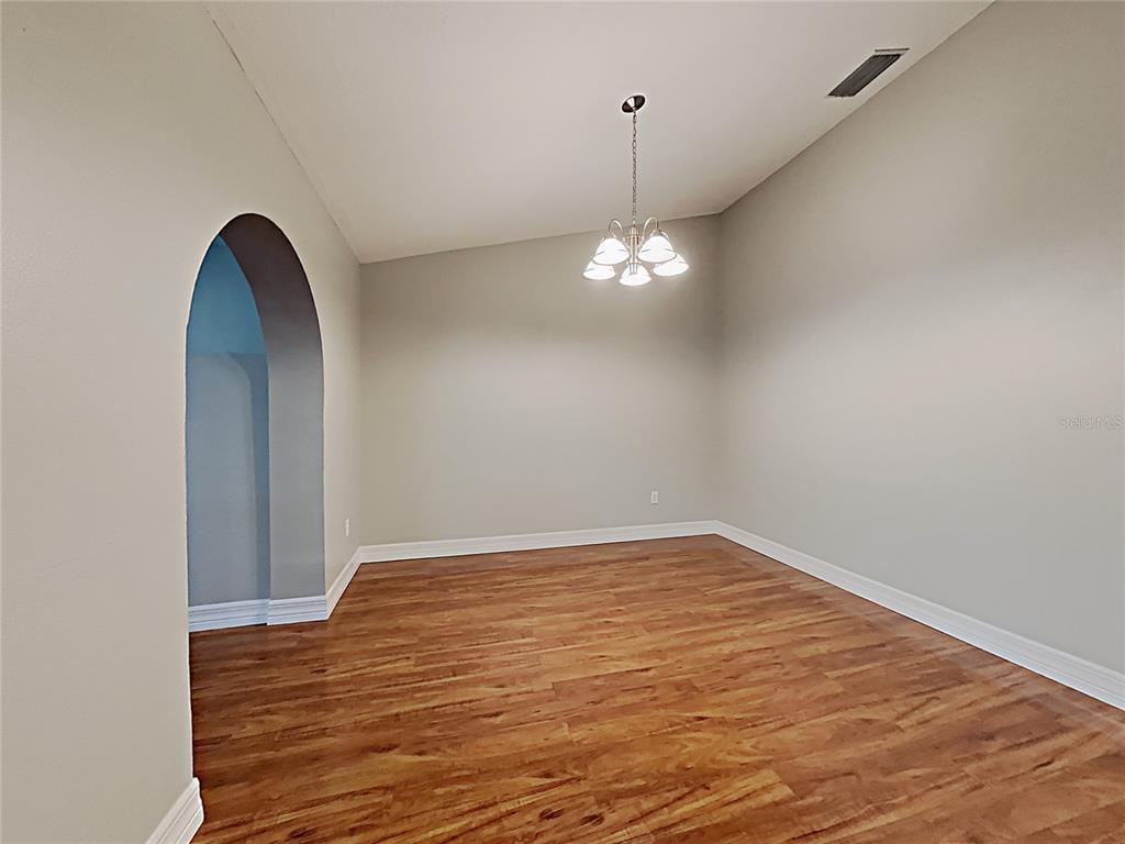 An empty dining room features wood-look flooring, light gray walls, a vaulted ceiling, and a chandelier — 1237 BARMERE LANE, BRANDON, FL