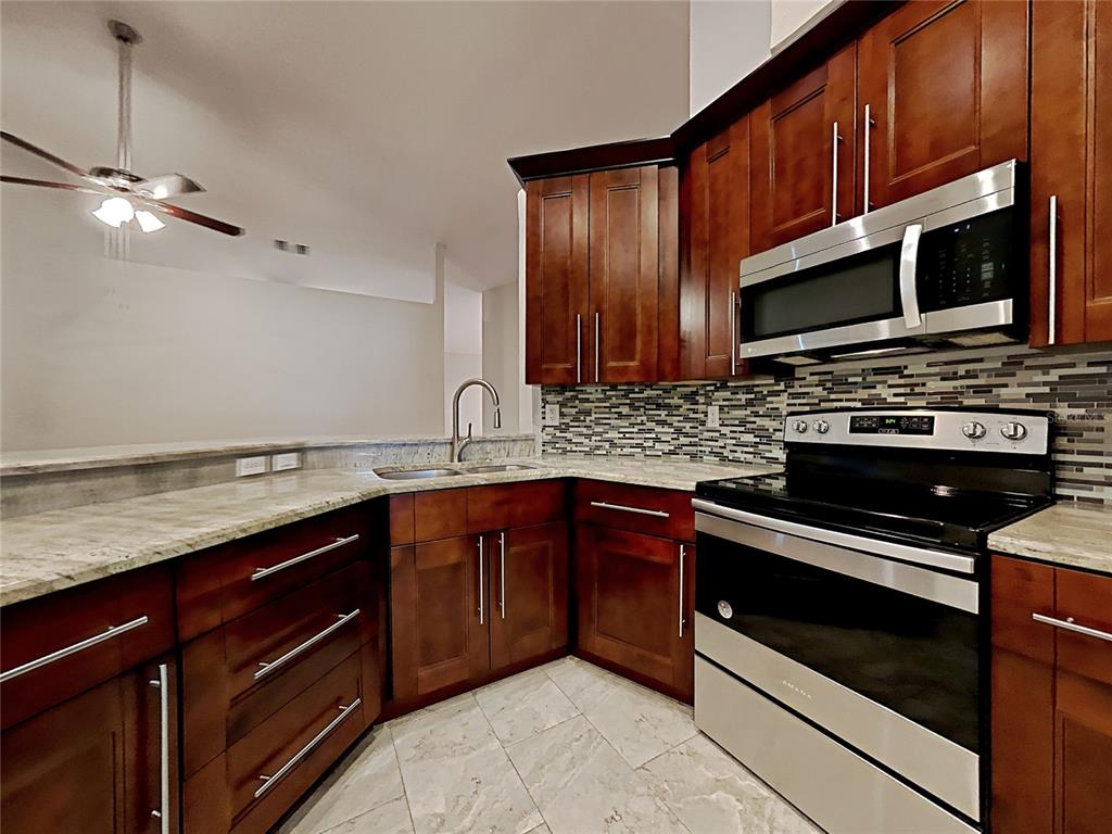 A kitchen with dark wood cabinets, granite countertops, stainless steel appliances, and a tiled backsplash — 1237 BARMERE LANE, BRANDON, FL