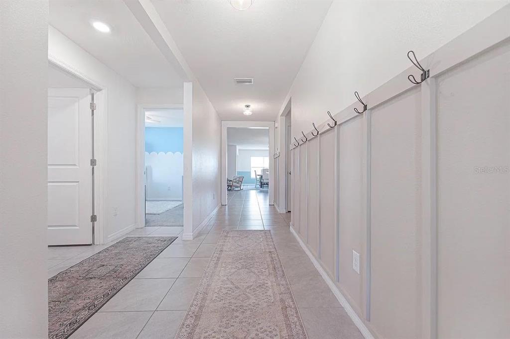 A hallway features light tile flooring, a runner rug, and a wall with coat hooks — 8574 TRIUMPH CIRCLE, WILDWOOD, FL