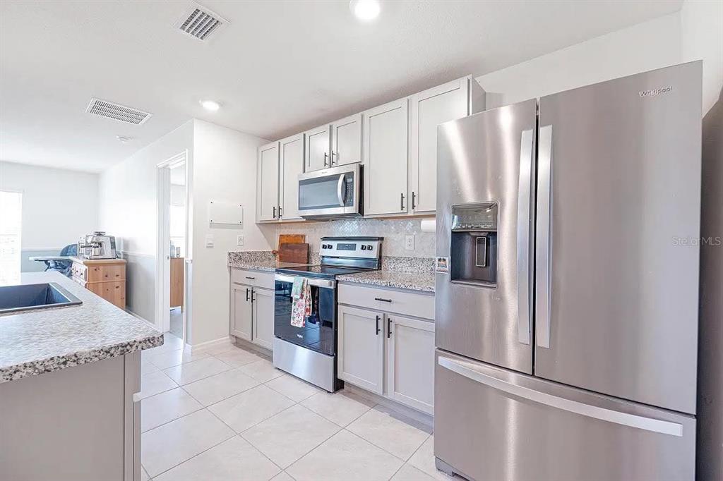 A kitchen features light gray cabinets, stainless steel appliances, granite countertops, and tile flooring — 8574 TRIUMPH CIRCLE, WILDWOOD, FL
