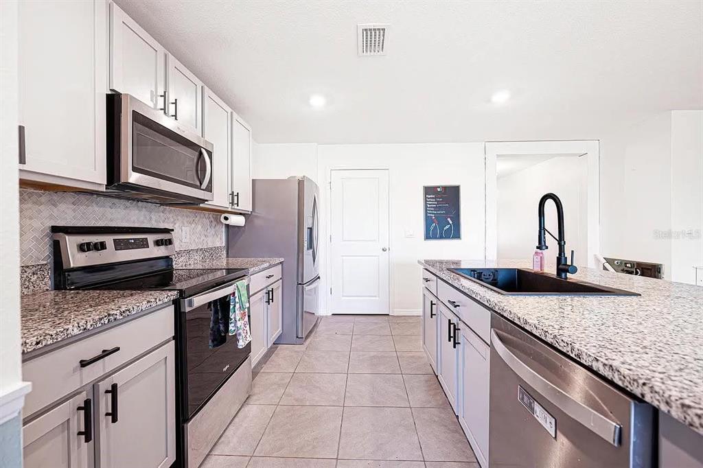 A modern kitchen features light gray cabinets, granite countertops, stainless steel appliances, and tile flooring — 8574 TRIUMPH CIRCLE, WILDWOOD, FL