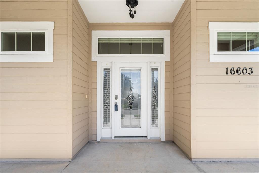 A tan house exterior features a white front door with glass panels and side windows — 16603 NW 168TH TERRACE, ALACHUA, FL