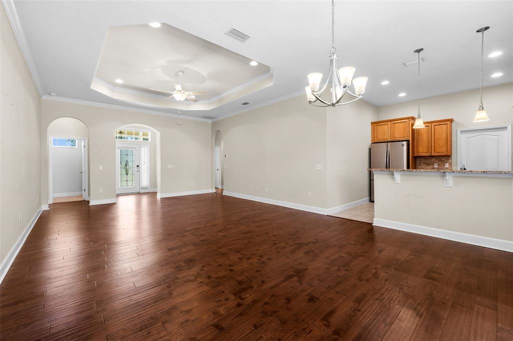 A spacious living room with dark wood flooring, a tray ceiling, and an open kitchen — 16603 NW 168TH TERRACE, ALACHUA, FL