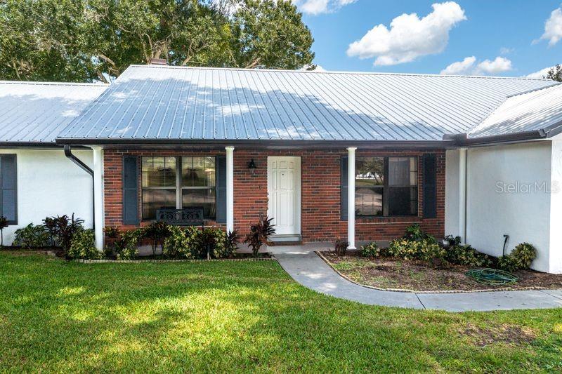 A single-story brick house features a metal roof, white columns, and a front walkway — 113 EARLS COURT, SEBRING, FL