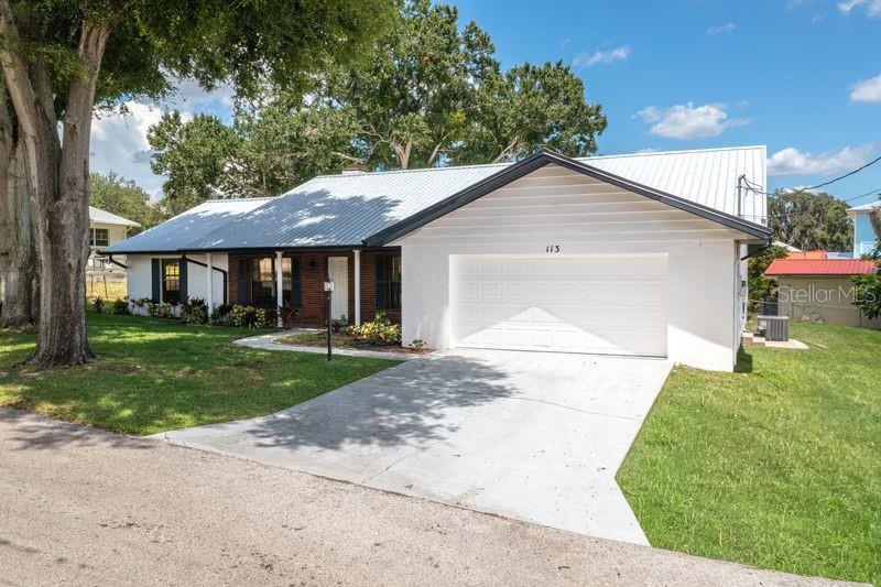 A white single-story house with a metal roof and a two-car garage — 113 EARLS COURT, SEBRING, FL