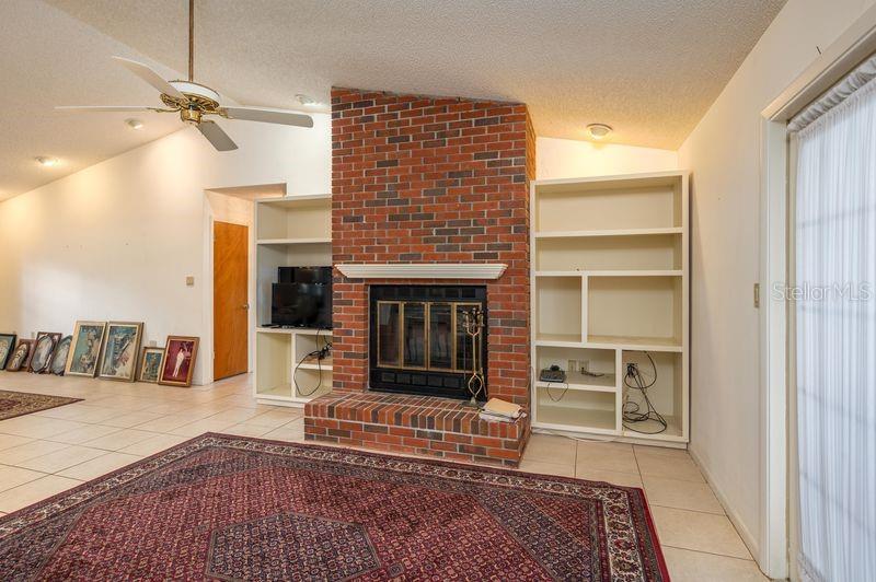 A living room features a red brick fireplace, built-in shelving, tile flooring, and a ceiling fan — 113 EARLS COURT, SEBRING, FL