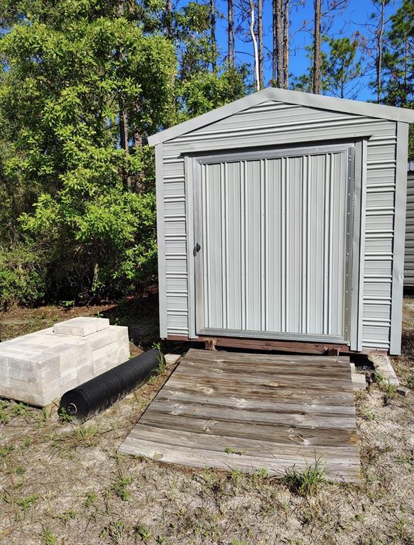 A metal storage shed sits on a wooden ramp in a wooded outdoor area — 5840 NW 11TH AVENUE, BELL, FL