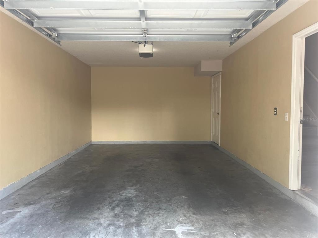 An empty two-car garage with tan walls, a concrete floor, and a white door — 341 SOUTHERN PECAN CIRCLE UNIT 201, WINTER GARDEN, FL