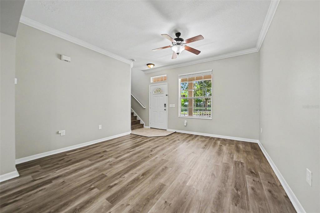 An empty living room features light gray walls, wood-look flooring, a ceiling fan, and stairs — 5579 SOMERSBY ROAD, WINDERMERE, FL