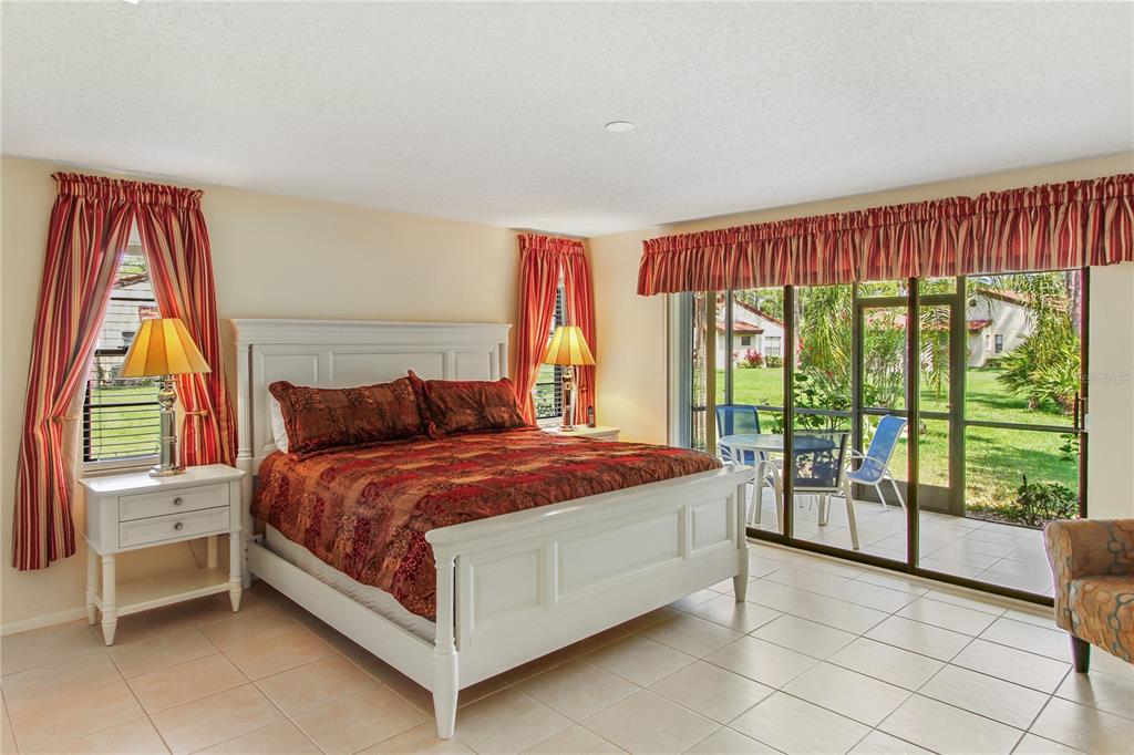 A bedroom with a white bed frame, tile flooring, and sliding glass doors to a patio — 3715 PINECONE COURT UNIT 169, SARASOTA, FL