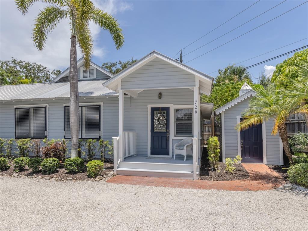 A light blue cottage features a covered front porch, a dark blue door, and landscaping — 726 EAGLE POINT DRIVE, VENICE, FL