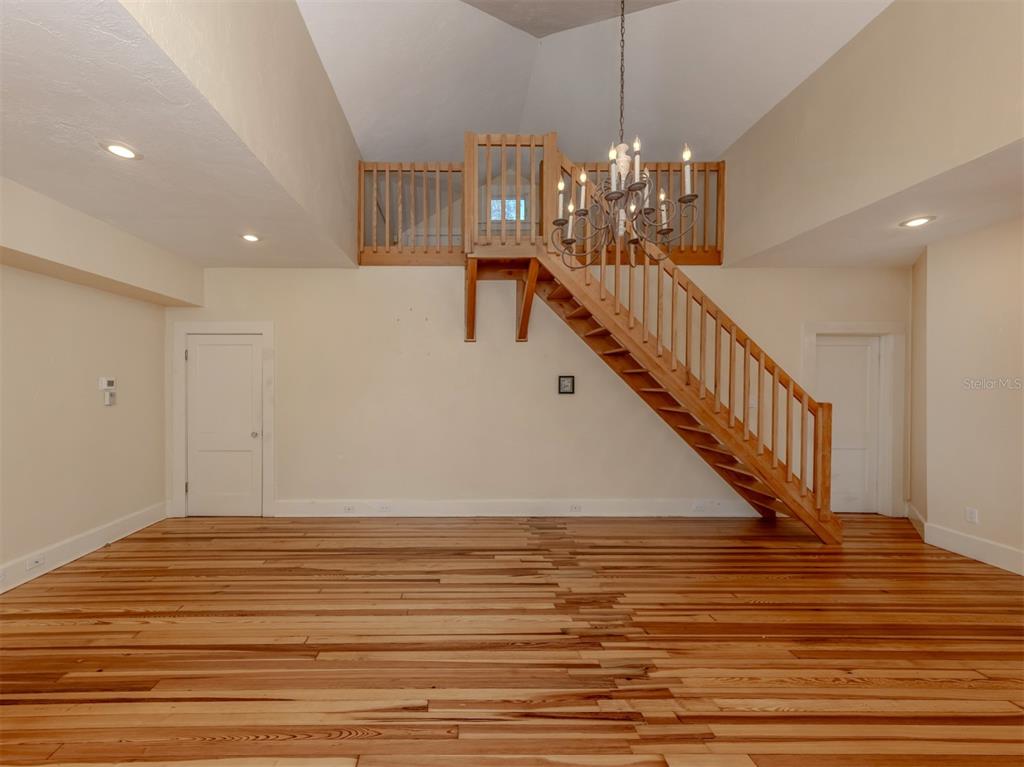 A room with hardwood floors, a wooden staircase, and a chandelier under a vaulted ceiling — 726 EAGLE POINT DRIVE, VENICE, FL