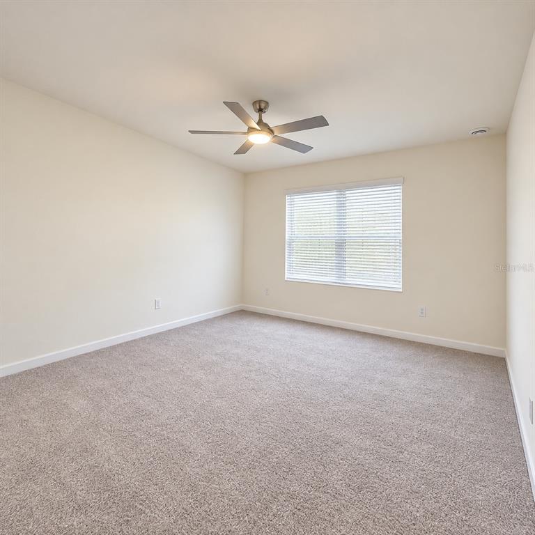 An empty bedroom features beige walls, neutral carpeting, a ceiling fan, and a window with blinds — 405 CHAYNE PLACE, ST CLOUD, FL