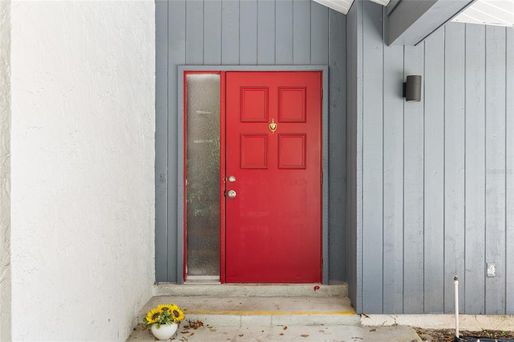 A red front door with a side window is set against gray vertical wood siding — 19 HOLLYHOCK COURT, HOMOSASSA, FL