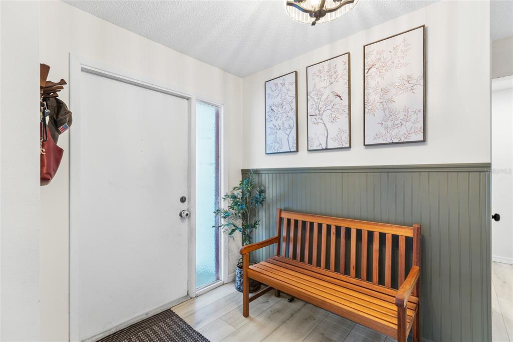 An entryway features a wooden bench, olive green wainscoting, and three framed botanical wall prints — 19 HOLLYHOCK COURT, HOMOSASSA, FL