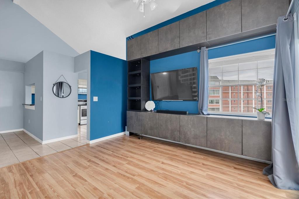 A living room features a blue accent wall, built-in gray cabinetry, a sectional sofa, and wood flooring — 6931 STONES THROW CIRCLE N UNIT 5302, ST PETERSBURG, FL