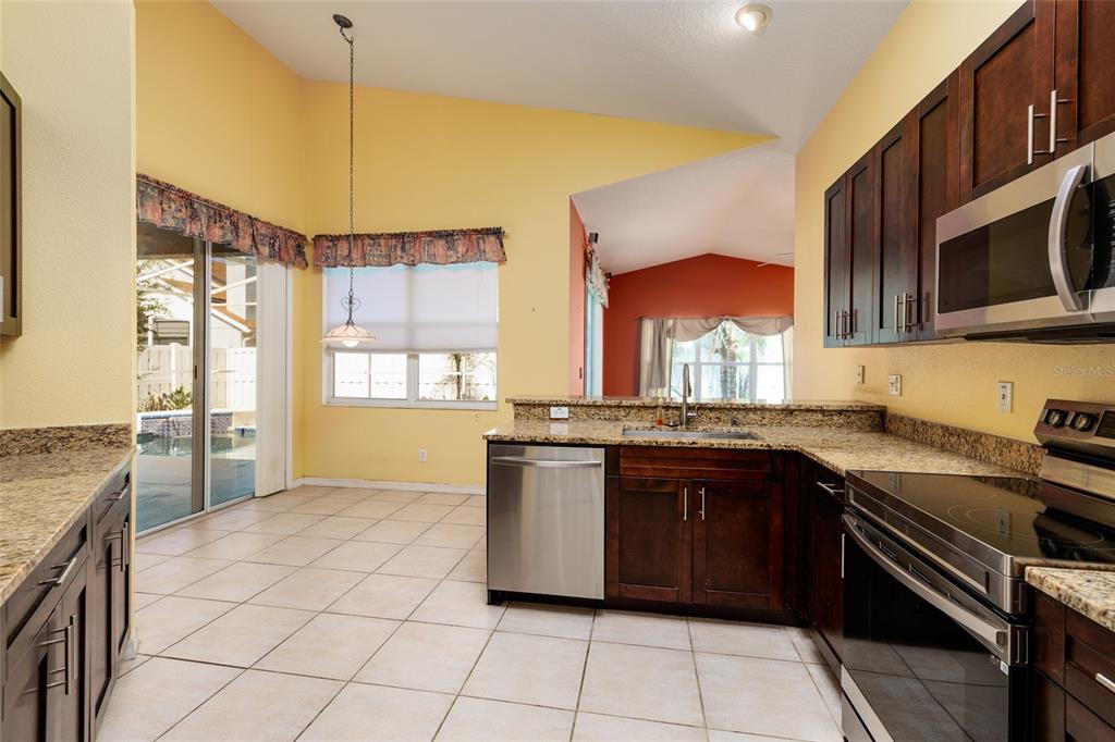 A kitchen with dark wood cabinets, granite countertops, stainless steel appliances, and tile flooring — 1805 WOOD BEND STREET, TARPON SPRINGS, FL