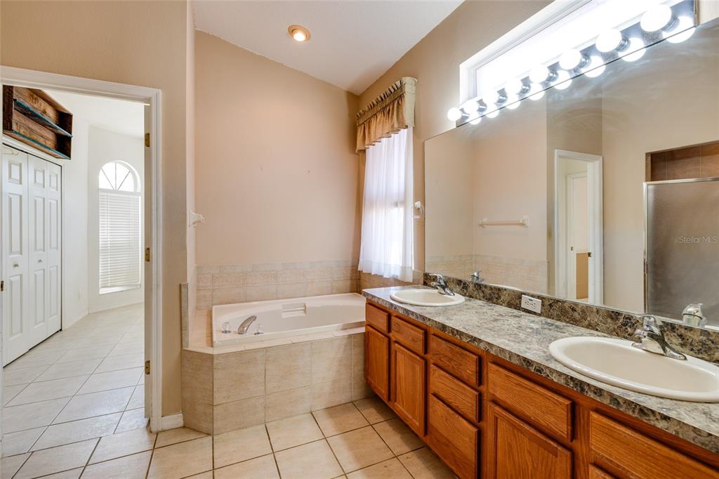 A bathroom features a double vanity with a stone countertop, a soaking tub, and tile flooring — 1805 WOOD BEND STREET, TARPON SPRINGS, FL