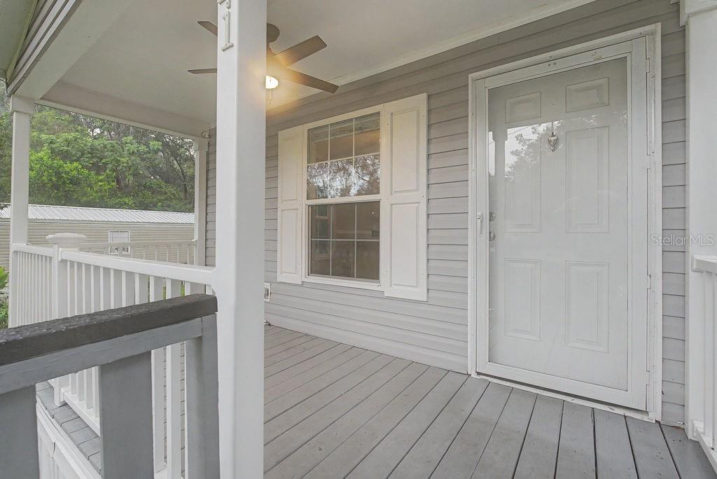 A gray wooden porch features a white front door, a window with shutters, and a ceiling fan — 641 MARSHBURN DRIVE, BRONSON, FL
