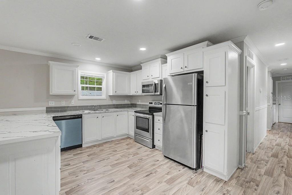 A kitchen features white cabinets, stainless steel appliances, marble-look countertops, and light wood-look flooring — 641 MARSHBURN DRIVE, BRONSON, FL
