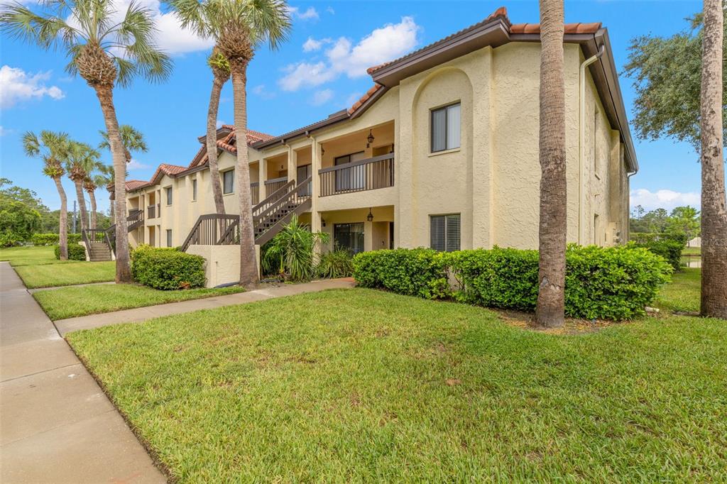 A two-story apartment building with stucco walls, a tiled roof, and an exterior staircase — 1801 E LAKE ROAD UNIT 19D, PALM HARBOR, FL