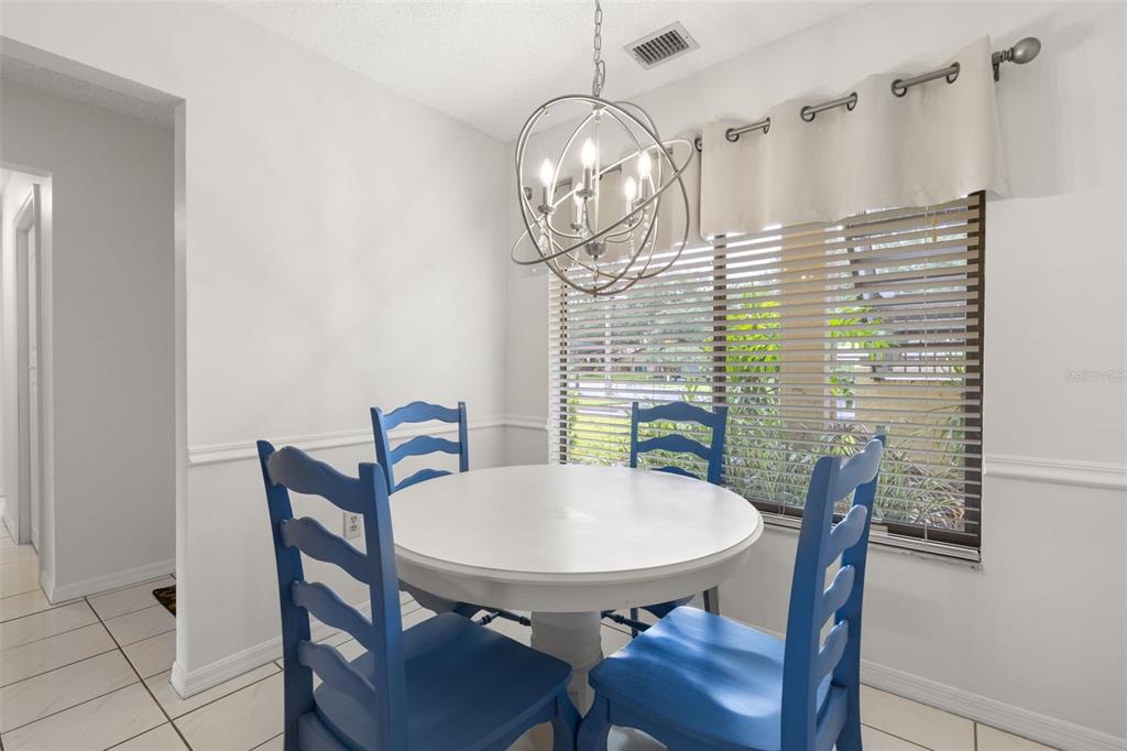 A dining area features a white round table, four blue chairs, and a modern orb chandelier — 1801 E LAKE ROAD UNIT 19D, PALM HARBOR, FL