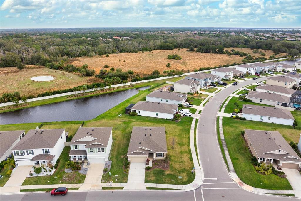 A screened-in patio with concrete flooring overlooks a grassy backyard and a distant pond — 431 158TH STREET E, BRADENTON, FL