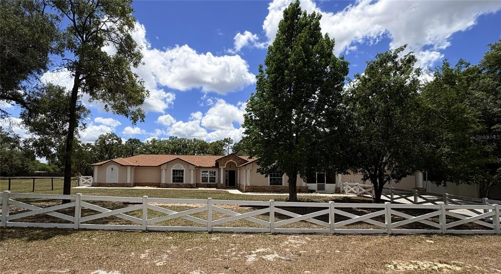 A single-story house with a tan exterior and a white fence in the foreground — 5085 BONE LANE, BROOKSVILLE, FL