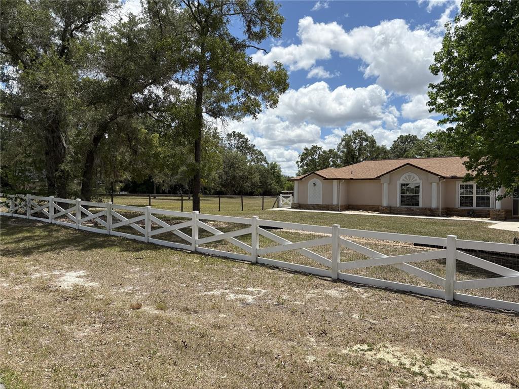 A white wooden cross-buck fence borders a grassy yard in front of a tan house — 5085 BONE LANE, BROOKSVILLE, FL