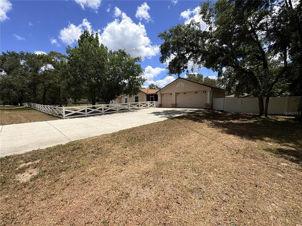 A beige house with a two-car garage and a white wooden fence in the yard — 5085 BONE LANE, BROOKSVILLE, FL