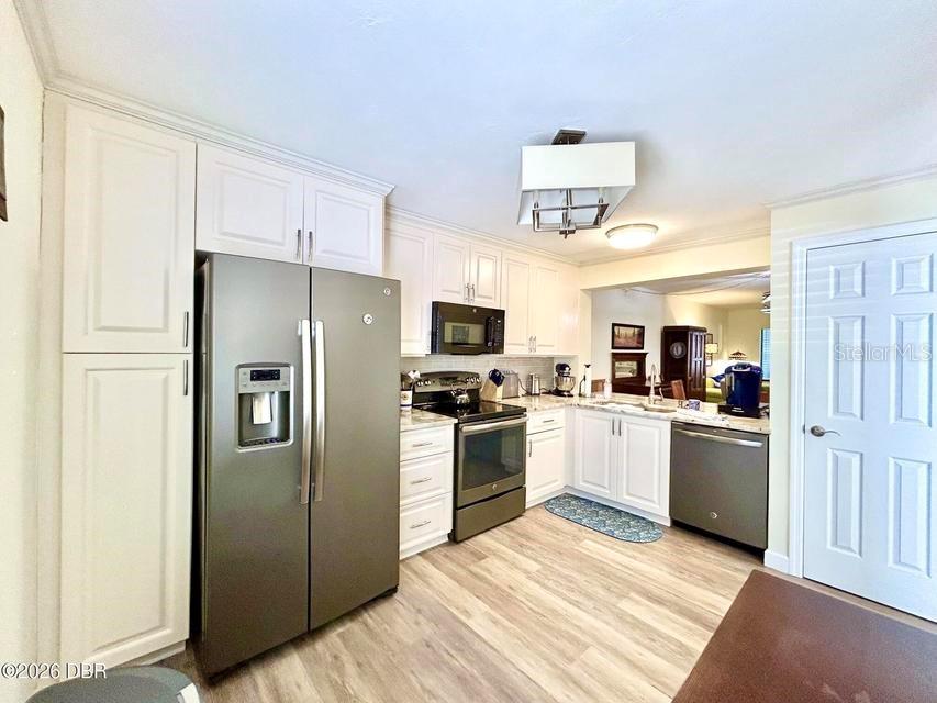 A kitchen features white cabinetry, stainless steel appliances, and light wood-look flooring — 1 TOMOKA OAKS BOULEVARD UNIT 119, ORMOND BEACH, FL